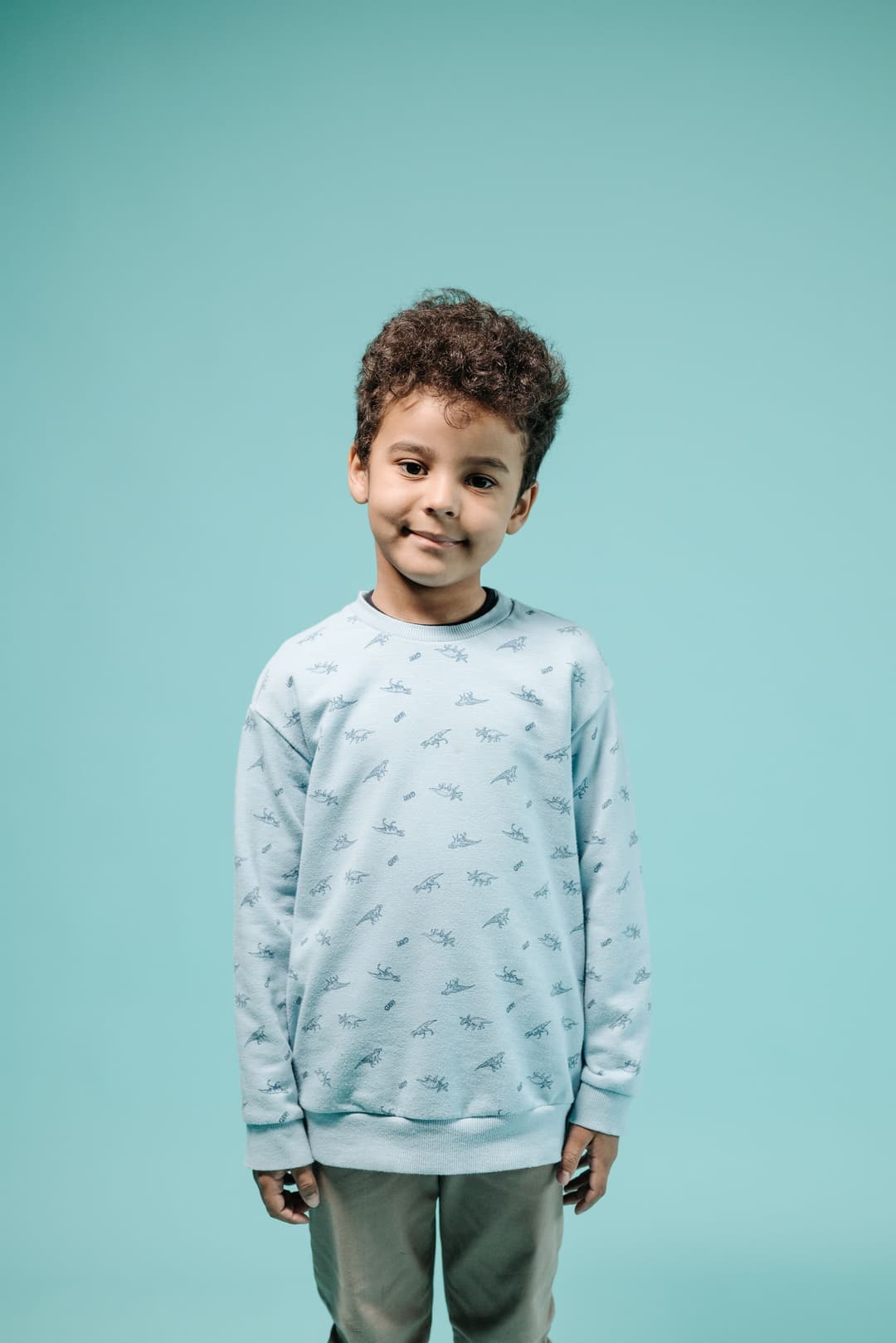 Child wearing a pale blue dinosaur-print sweatshirt