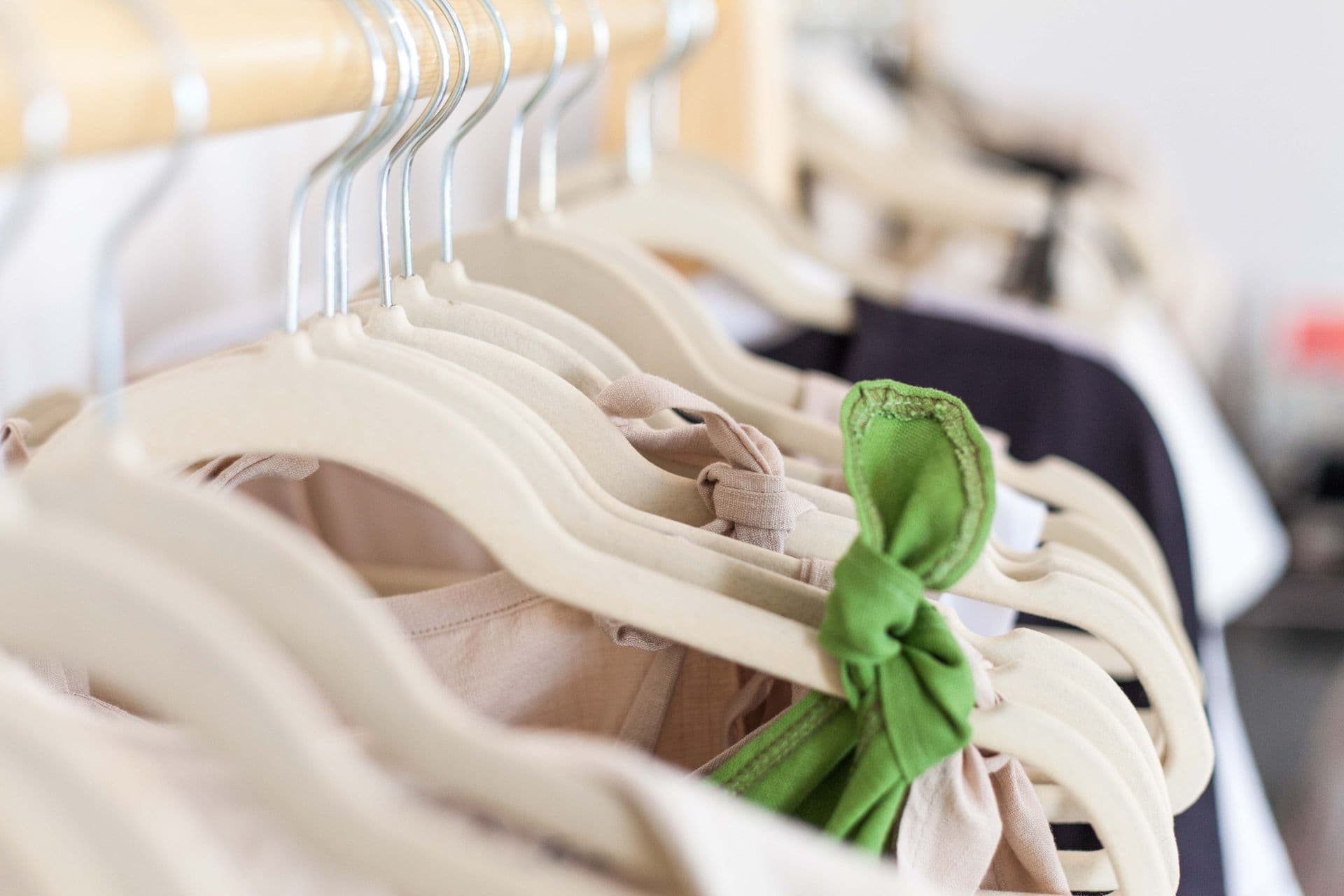 A row of natural-cotton garments on wooden hangers, one knotted with a green tie