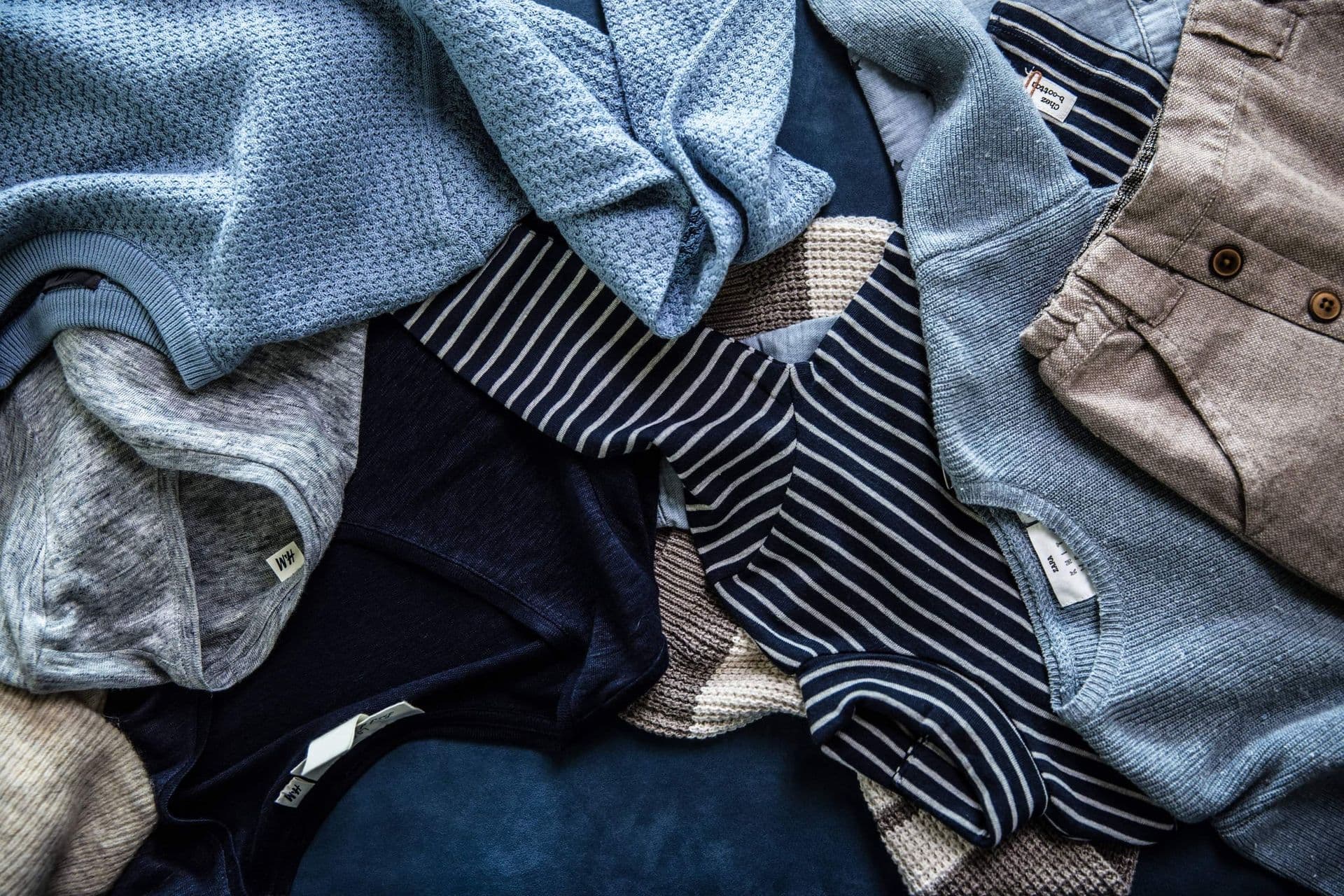 A flat-lay pile of folded knitwear in blues, greys and stone