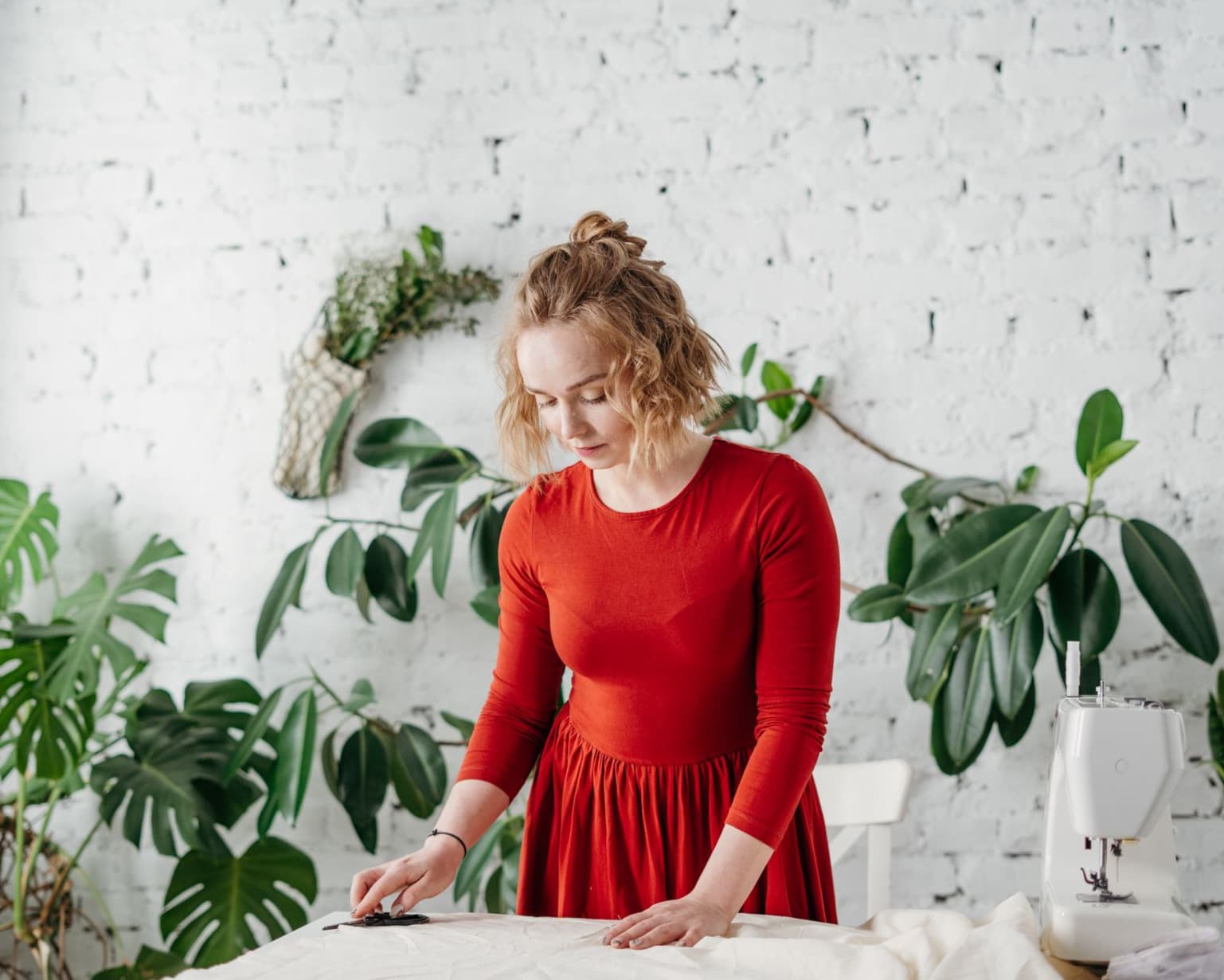 A maker marking out fabric on a cutting table in a plant-filled studio