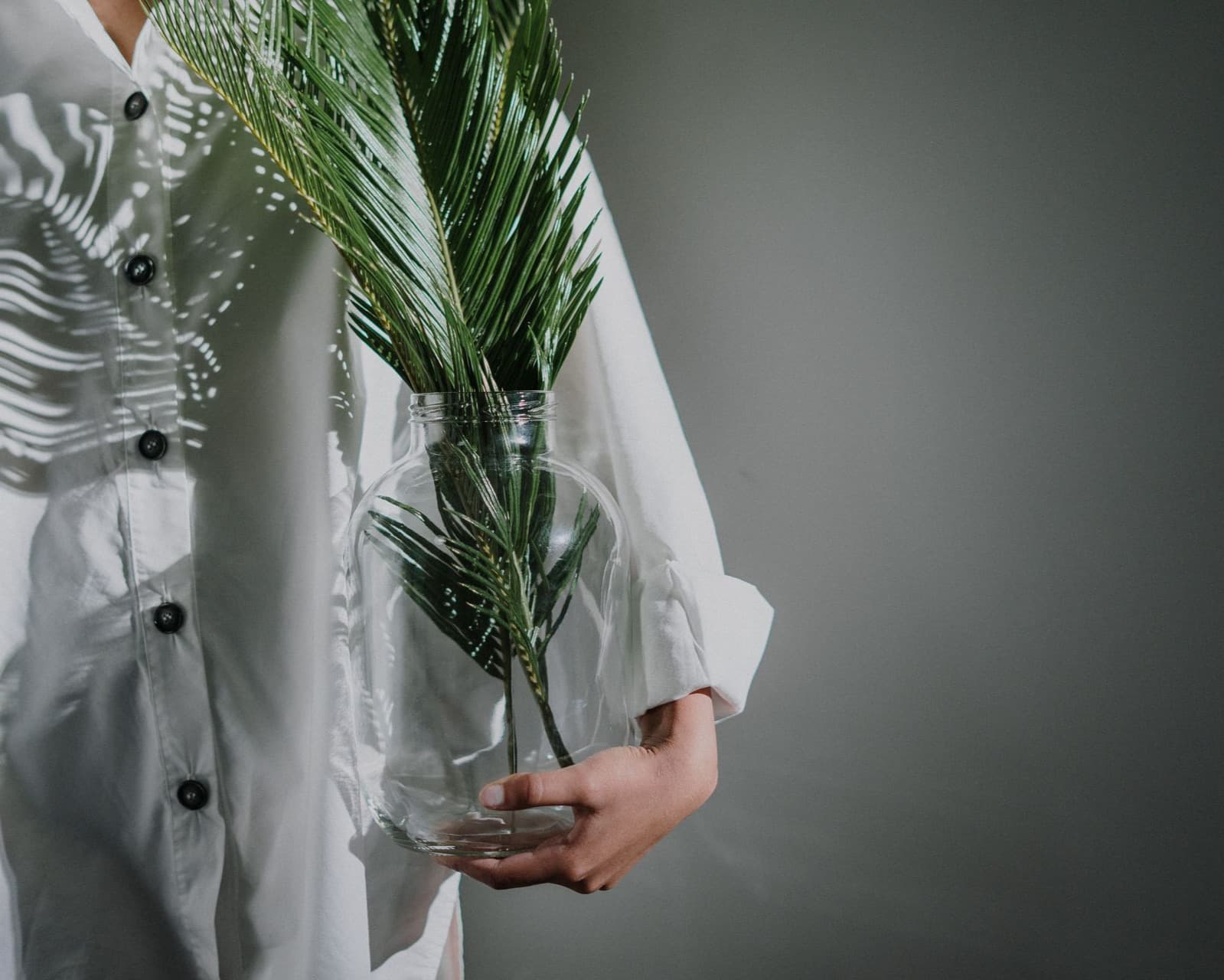 A person in a white cotton shirt holding a glass jar with a palm frond