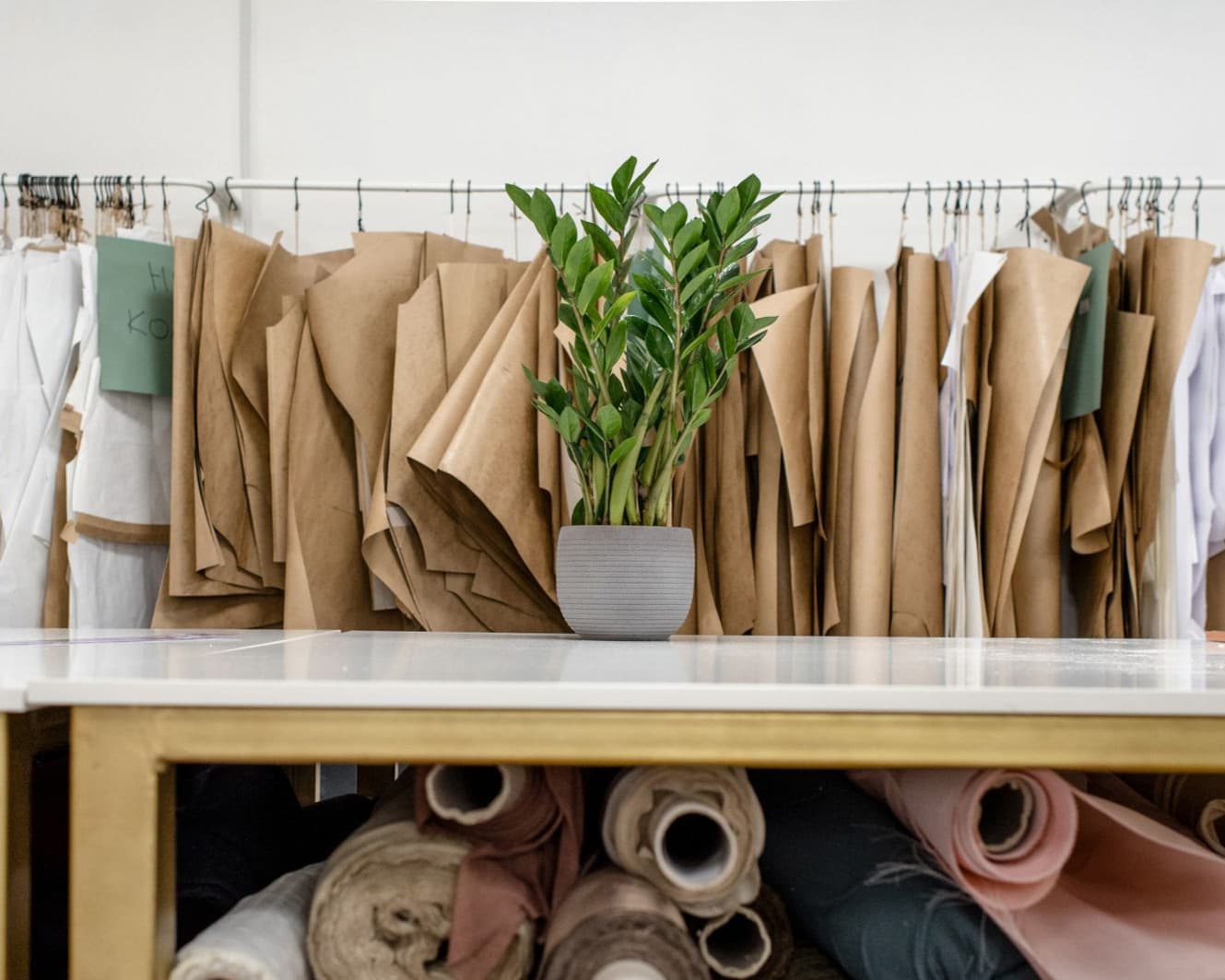 Bolts of fabric racked beneath a cutting table, pattern paper hanging on a rail behind