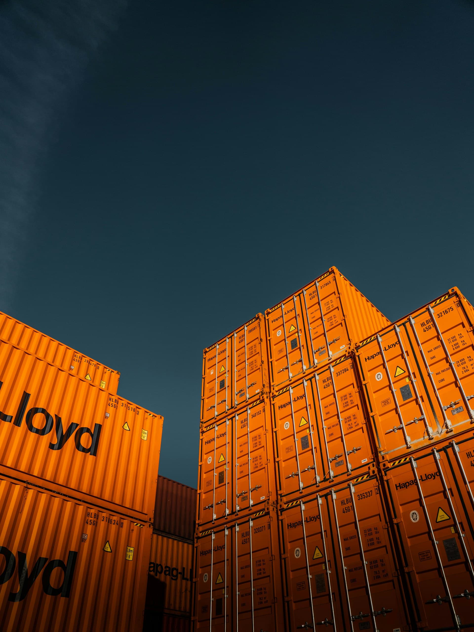 Stacked shipping containers lit orange against a deep blue dusk sky