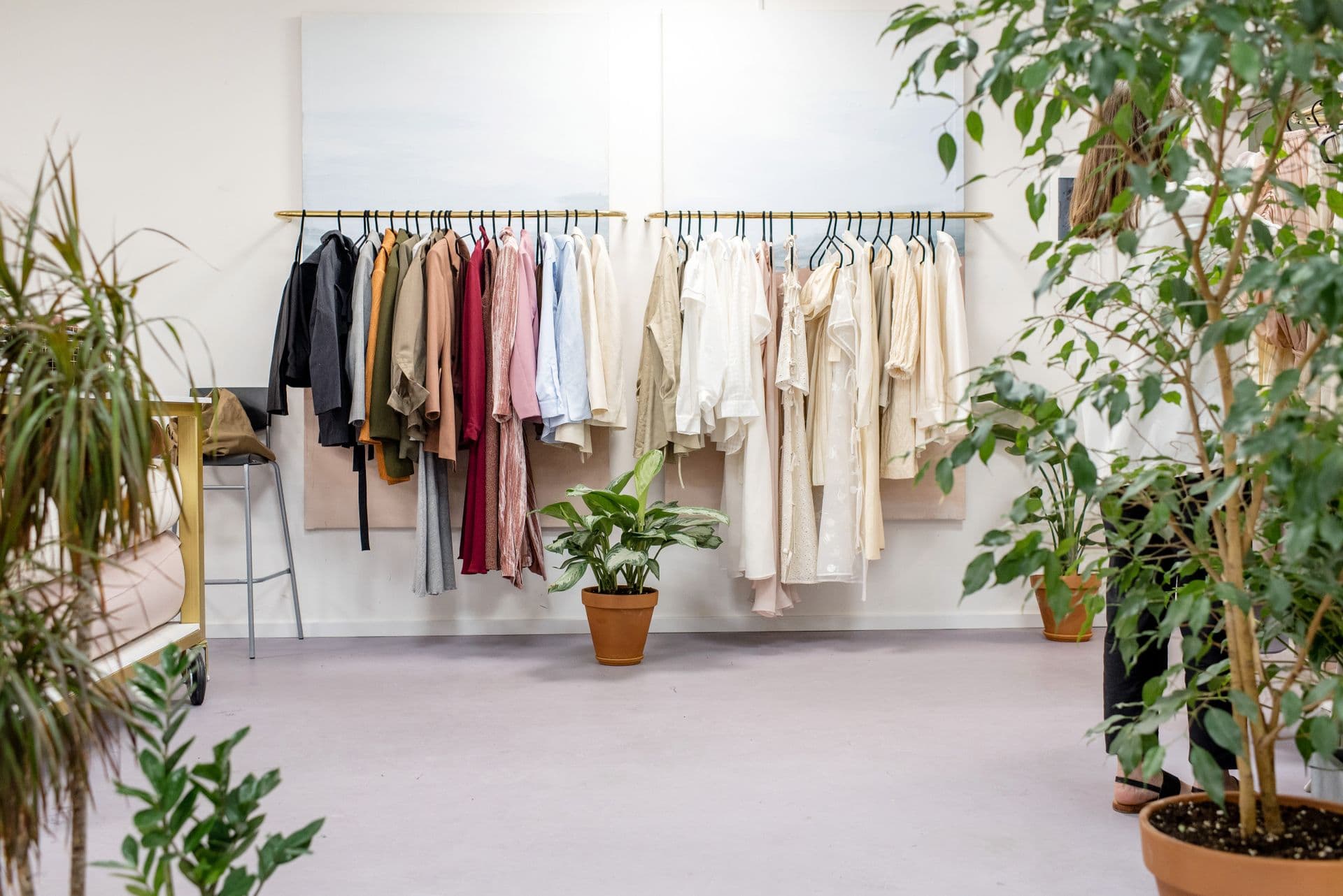 Two rails of garments on a white studio wall, framed by potted trees and plants