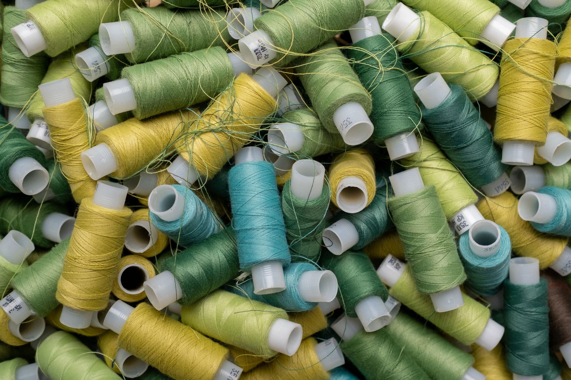 A heap of sewing thread spools in greens, yellows and teal
